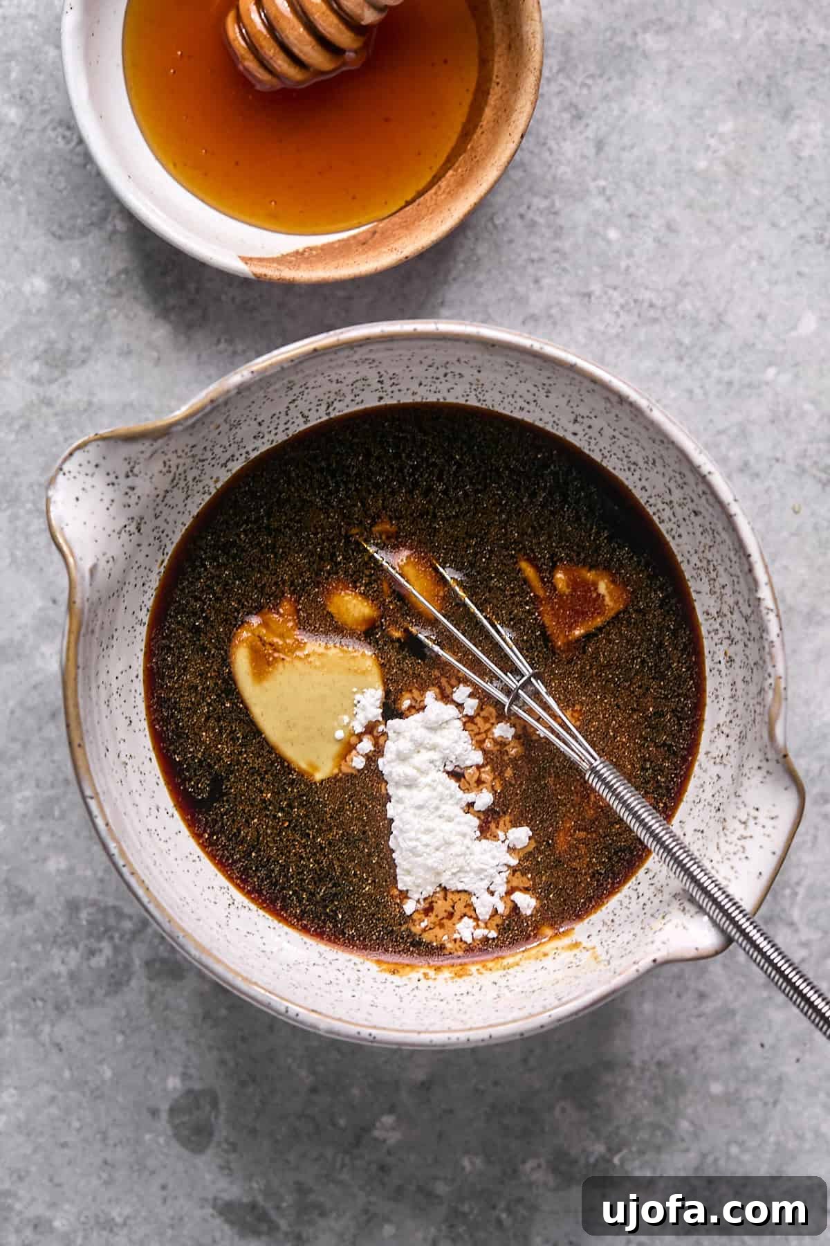 Ingredients for hot honey sauce, including coconut aminos, Dijon, hot honey, and spices, combined in a small bowl with a whisk.