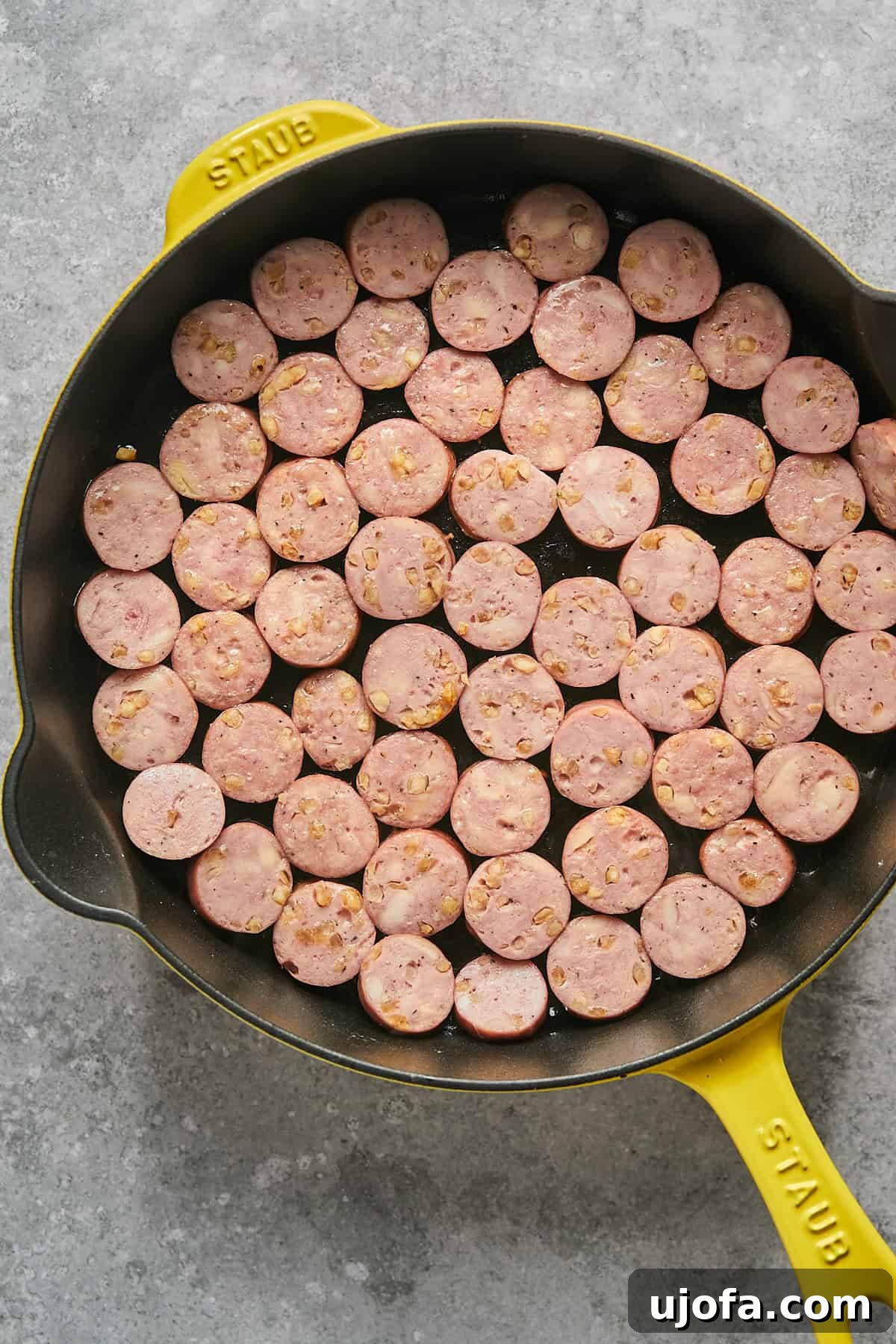 Sliced pre-cooked chicken sausages browning in a single layer in a yellow Staub skillet.