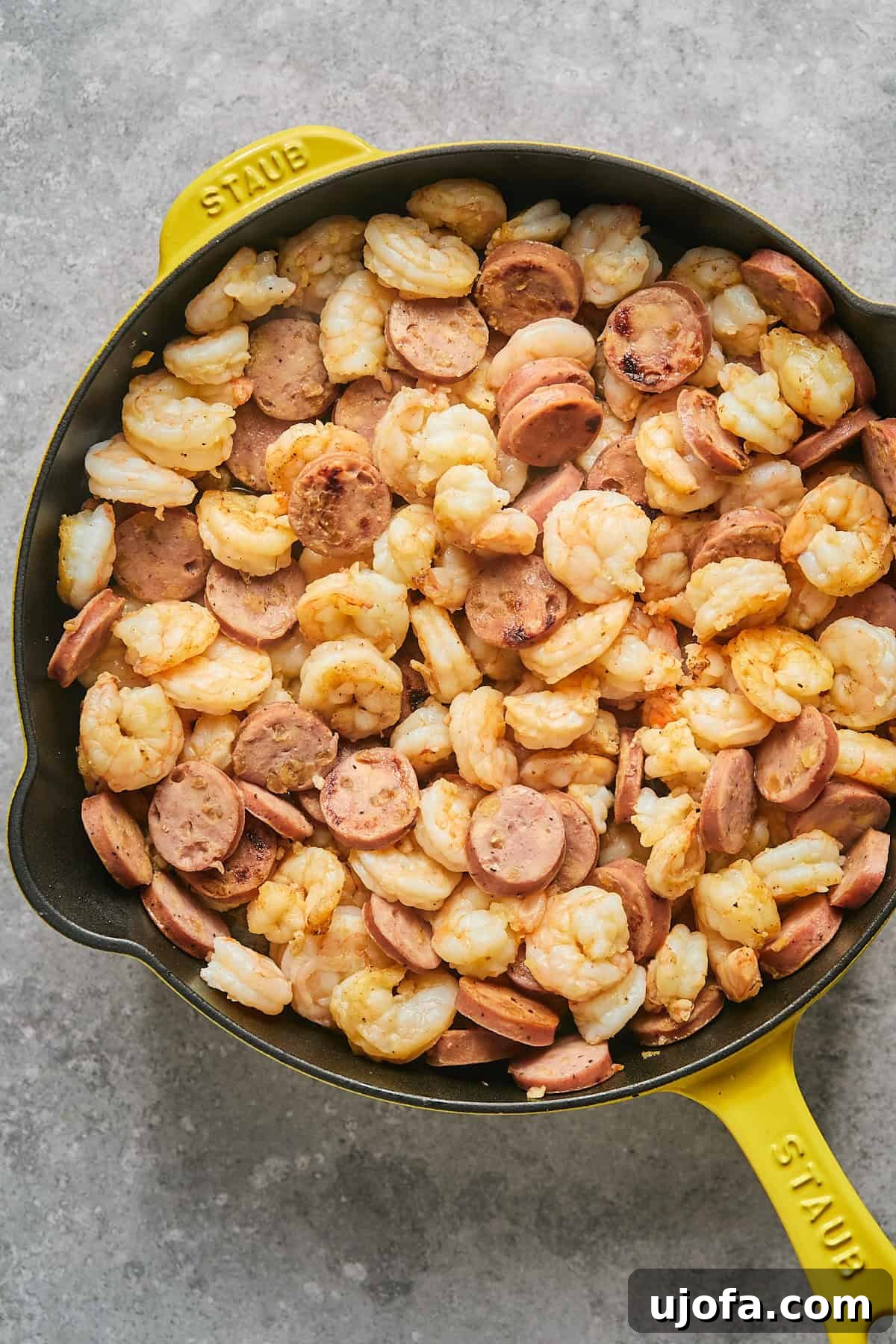 Shrimp and chicken sausage cooking together in a yellow skillet, sizzling beautifully.