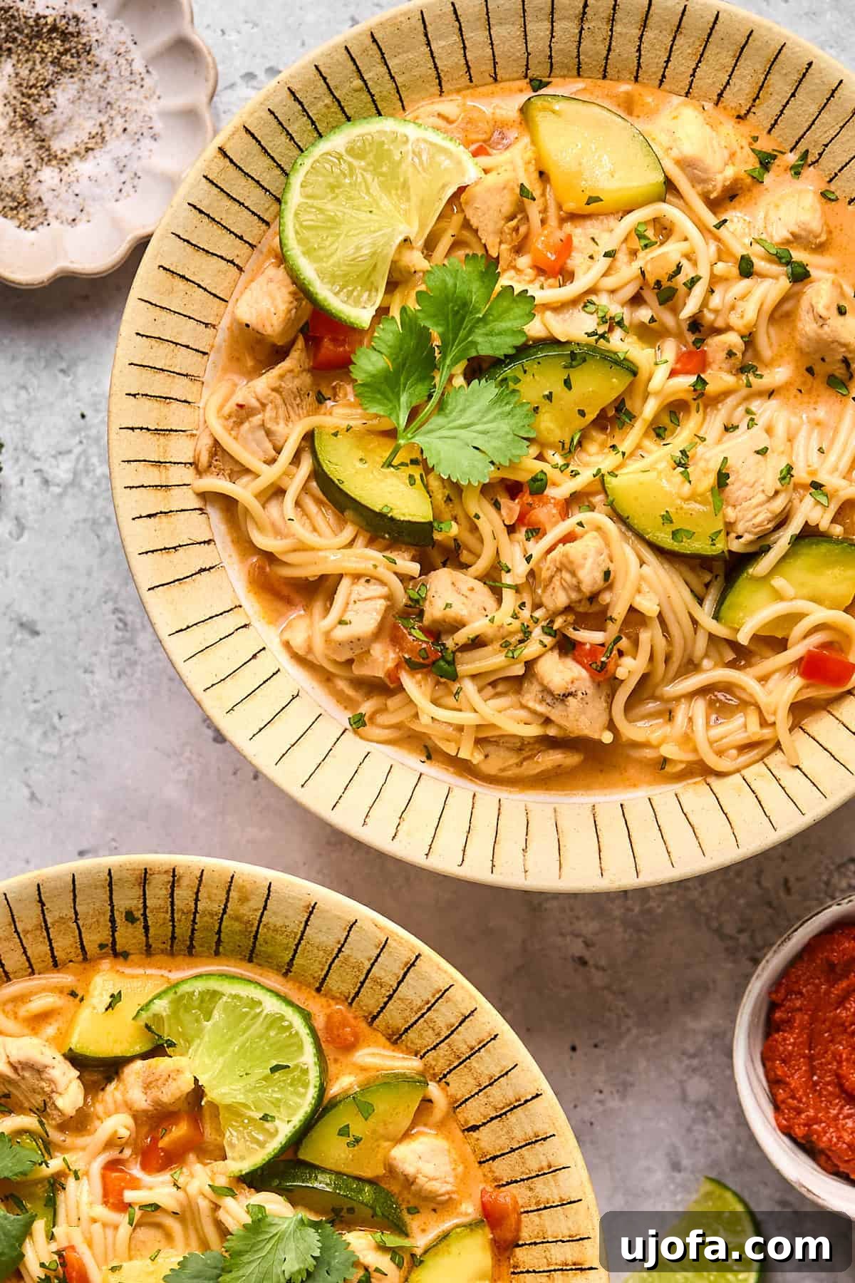 An overhead shot of red curry soup with noodles in a bowl, garnished with fresh cilantro and a lime wedge, ready to be enjoyed.