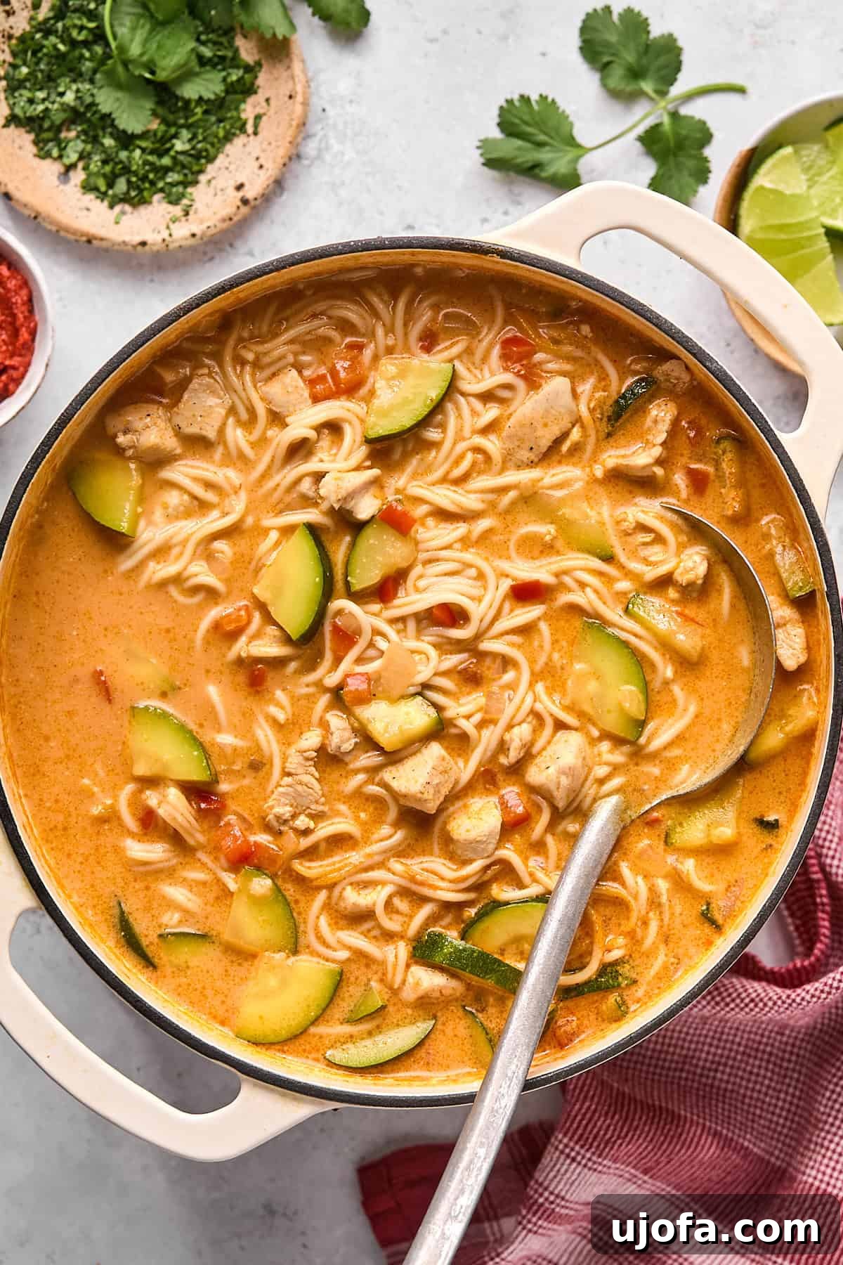 A large pot of finished Thai noodle soup, rich and creamy, with a serving ladle resting inside, ready to be dished out and enjoyed.