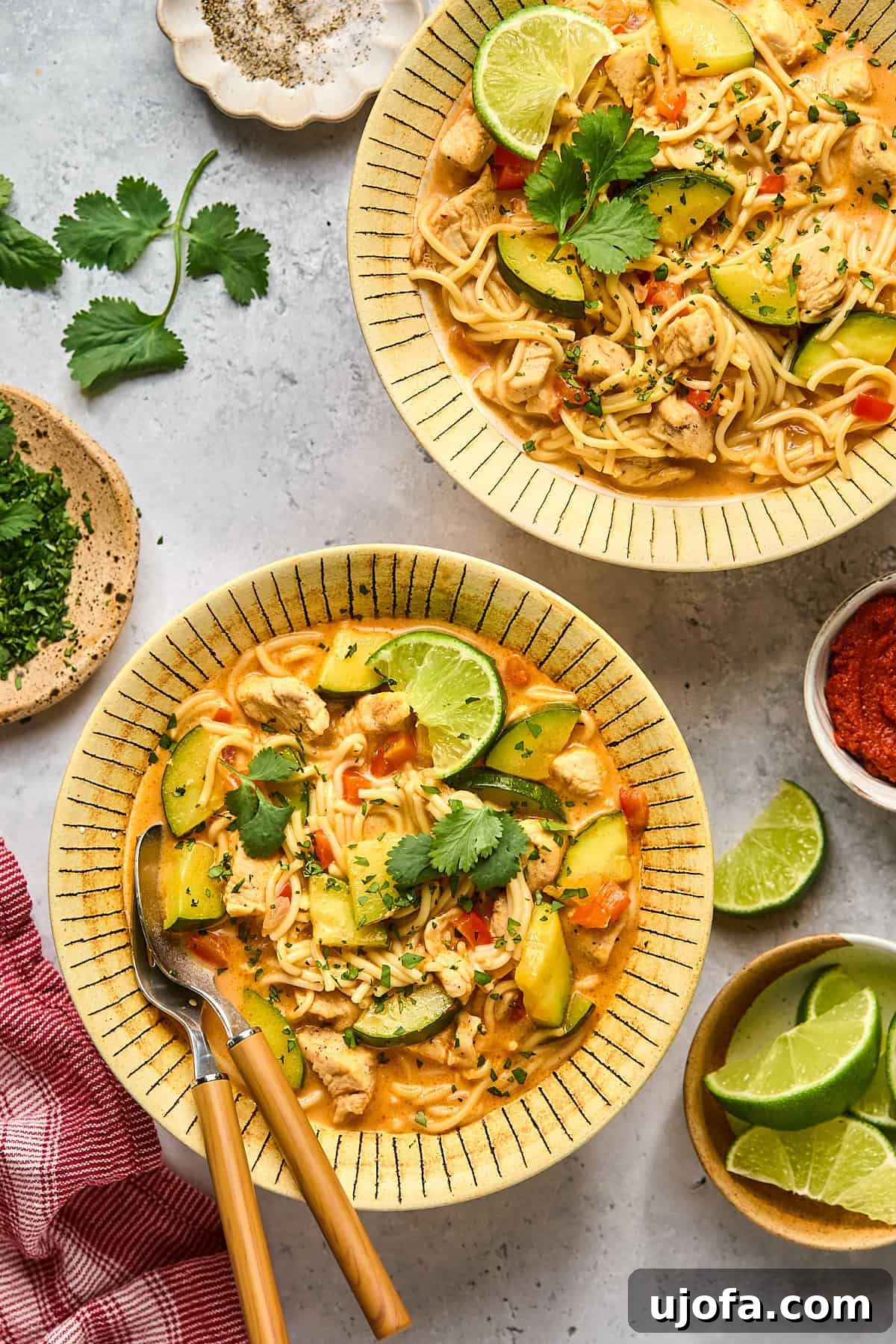 Two bowls of vibrant red curry soup, garnished with fresh lime wedges and cilantro, presented against a rustic background.