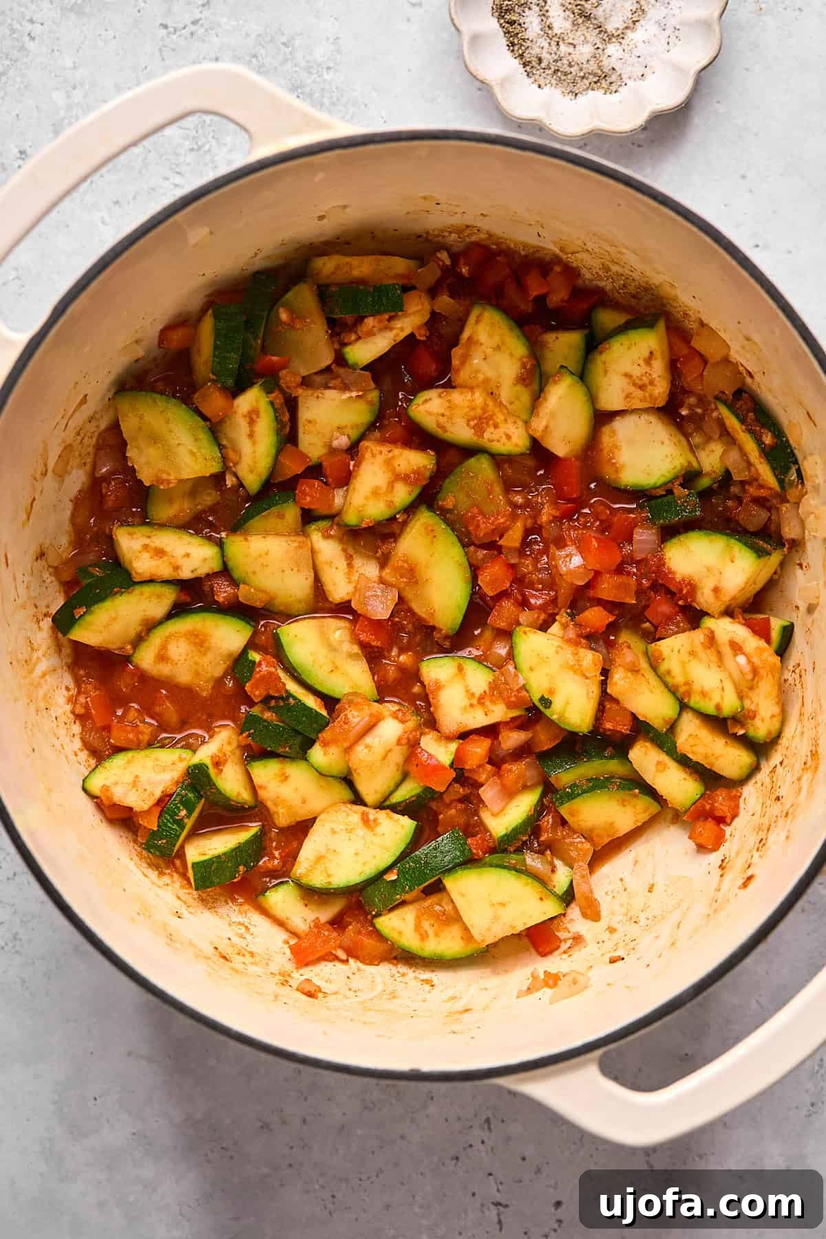 Sautéed vegetables mixed with fragrant Thai red curry paste and grated fresh ginger in a pot, releasing their aromatic spices.