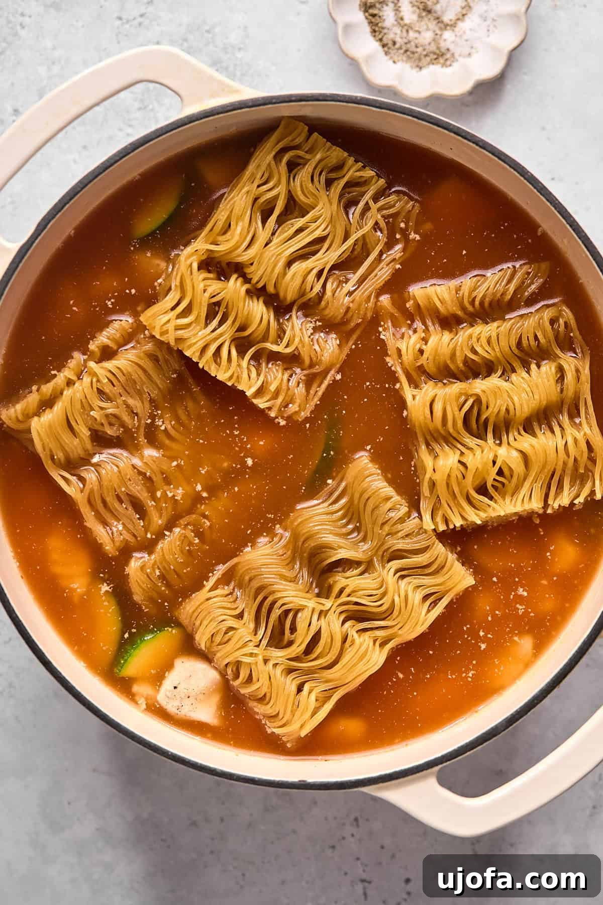 Cooked chicken, chicken broth, and rice ramen noodles added to the pot with the sautéed vegetables and curry paste, ready to simmer.