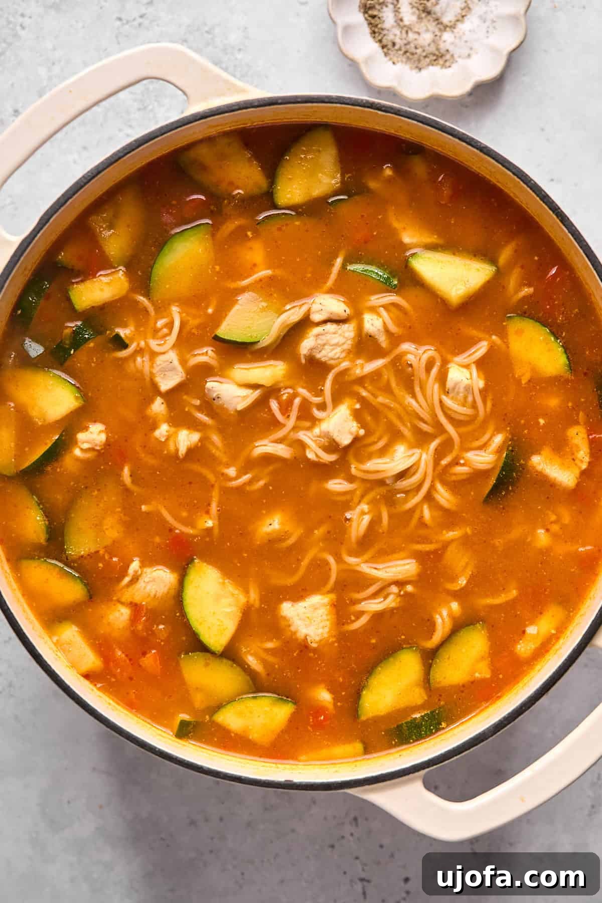 Thai noodle soup simmering in a pot with softened rice ramen noodles and tender zucchini, absorbing the rich flavors of the broth.