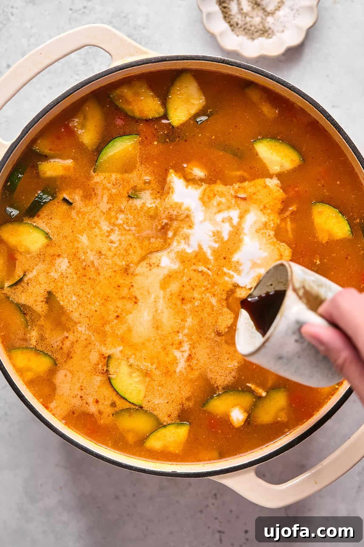 Creamy full-fat coconut milk being poured into the simmering Thai soup, along with coconut aminos and fresh lime juice, to enrich the broth.