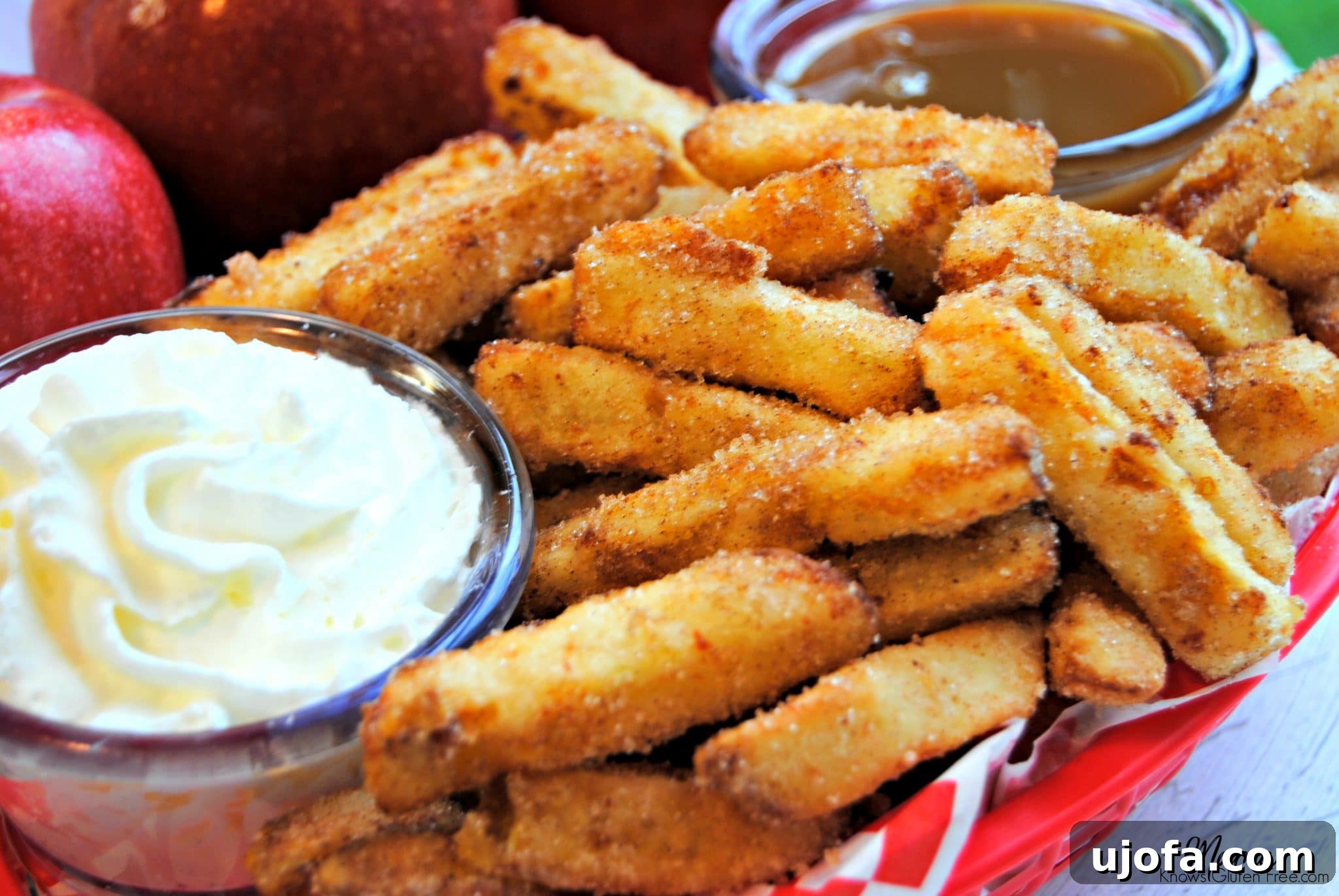 Cinnamon Spiced Apple Fries Gluten Free Dairy Free 3 Crispy cinnamon apple fries piled high in a rustic basket, accompanied by generous dollops of whipped cream and a rich caramel dipping sauce. Fresh red apples are visible in the soft-focus background, hinting at the natural goodness of this homemade dessert.