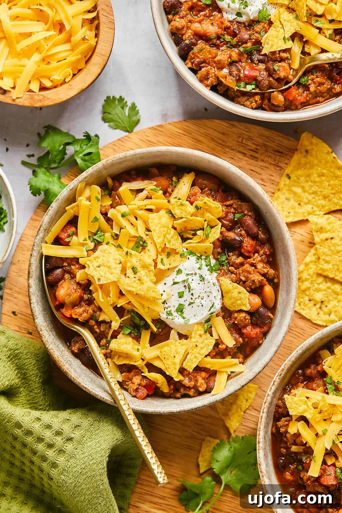 Ultimate Slow Cooker Taco Chili Recipe 12 The top view of a bowl of rich chili adorned with a generous sprinkle of corn chips, a dollop of sour cream, and fresh cilantro, with a spoon resting invitingly on the side.