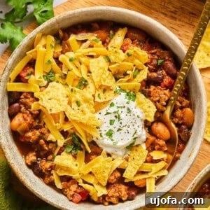A bowl of taco chili topped with crushed chips, sour cream, and cheese, showcasing the finished dish.