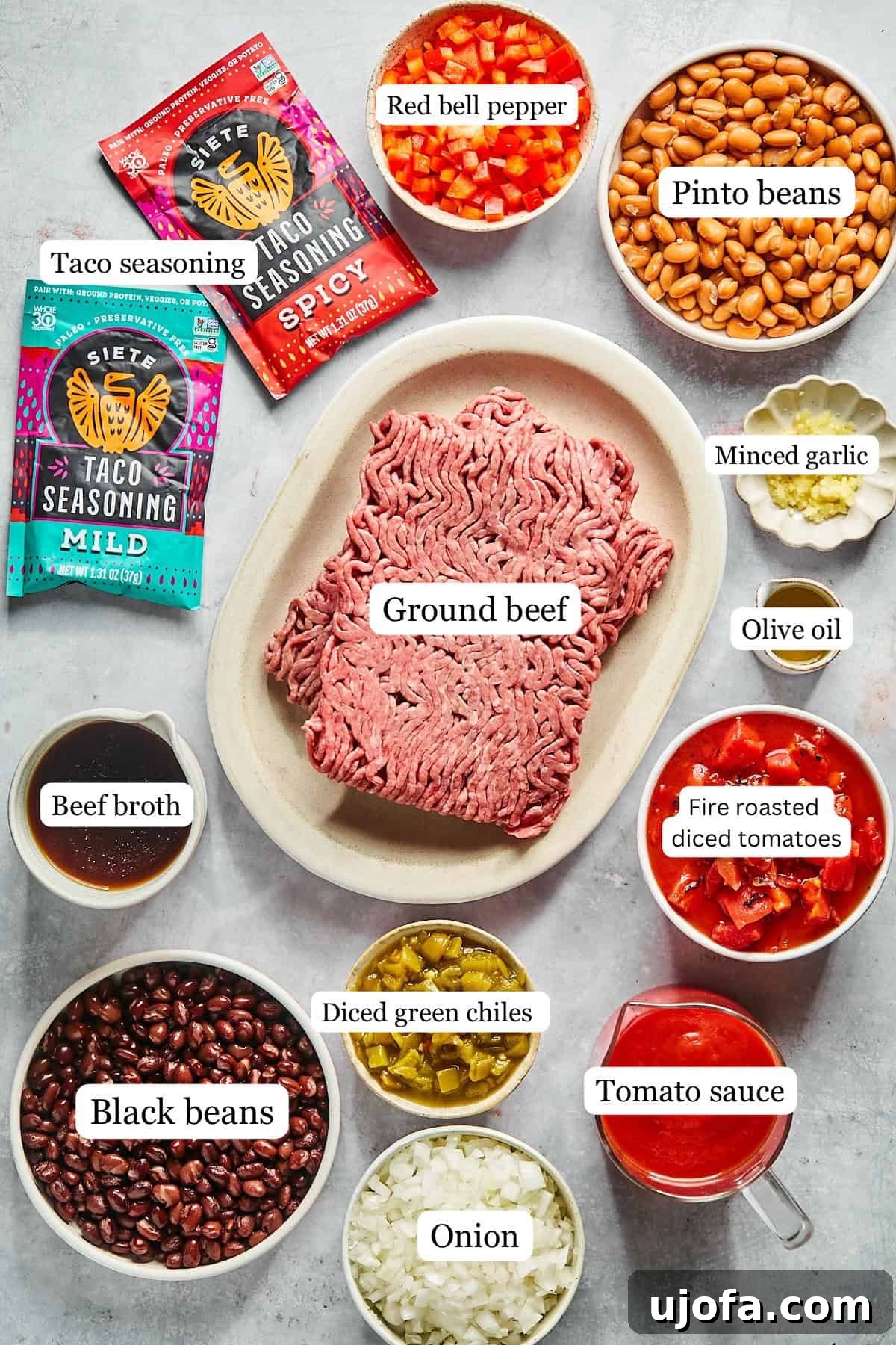 Ultimate Slow Cooker Taco Chili Recipe 3 Small bowls containing labeled recipe ingredients like olive oil, ground beef, diced onions, bell peppers, garlic, various beans, and spices, all neatly arranged for cooking.