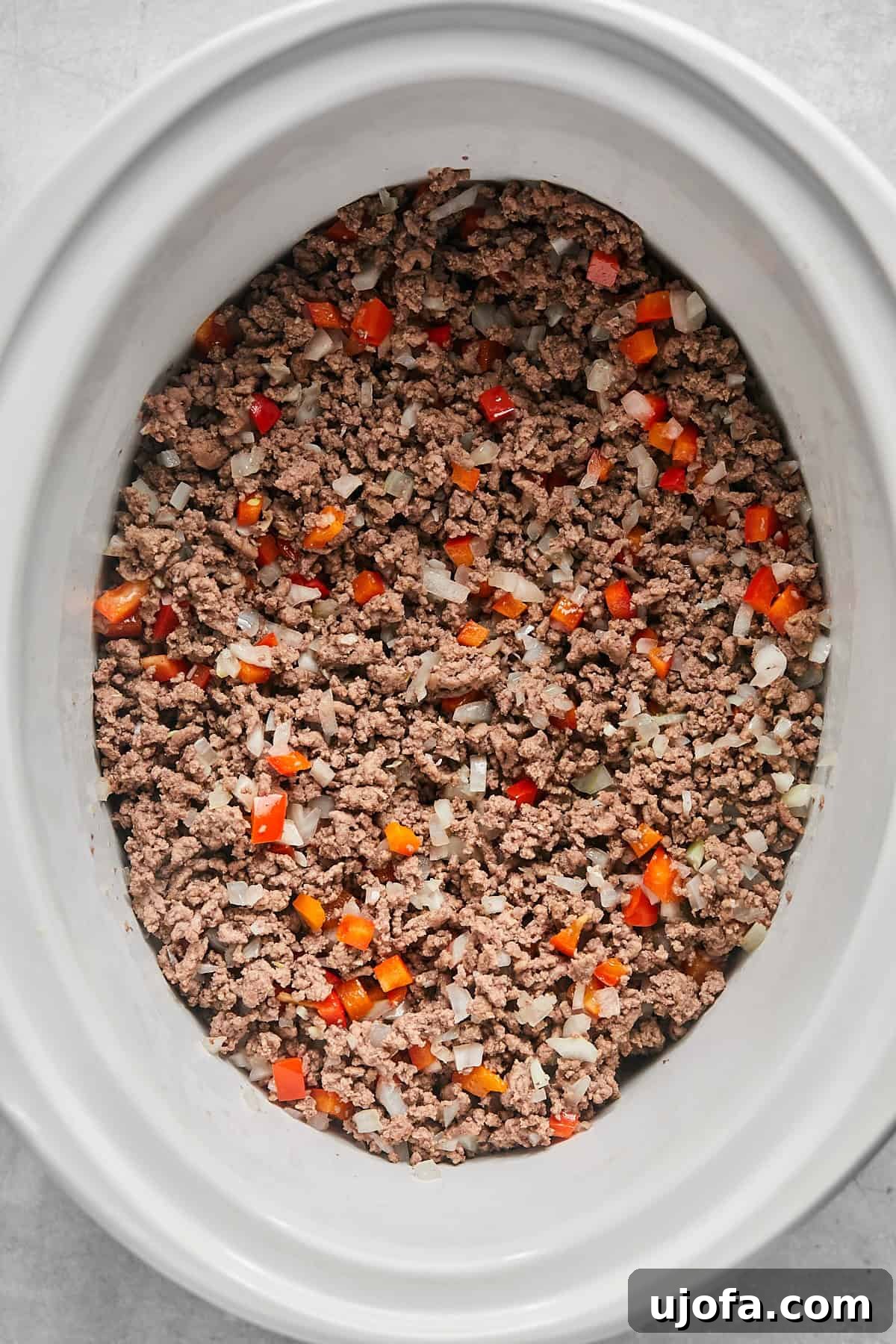 Ultimate Slow Cooker Taco Chili Recipe 6 The cooked ground beef and sautéed vegetable mixture being transferred into a white slow cooker, ready for the remaining ingredients.