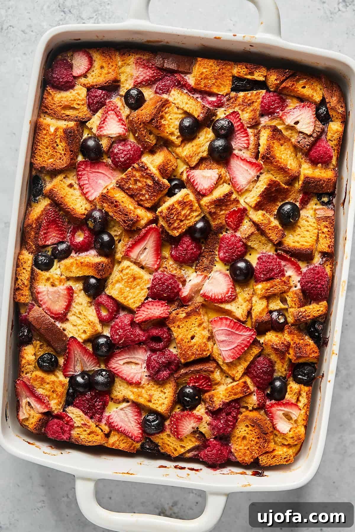 Baked Protein French Toast Casserole, golden brown and bubbly, adorned with a vibrant array of berries in a baking dish.