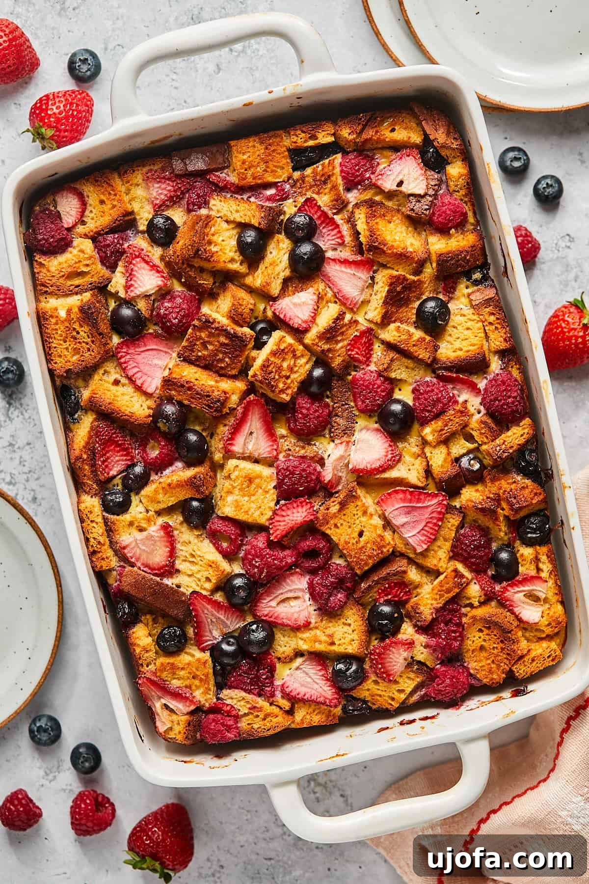 A vibrant casserole dish brimming with golden-brown French toast, adorned with a colorful array of fresh sliced berries.