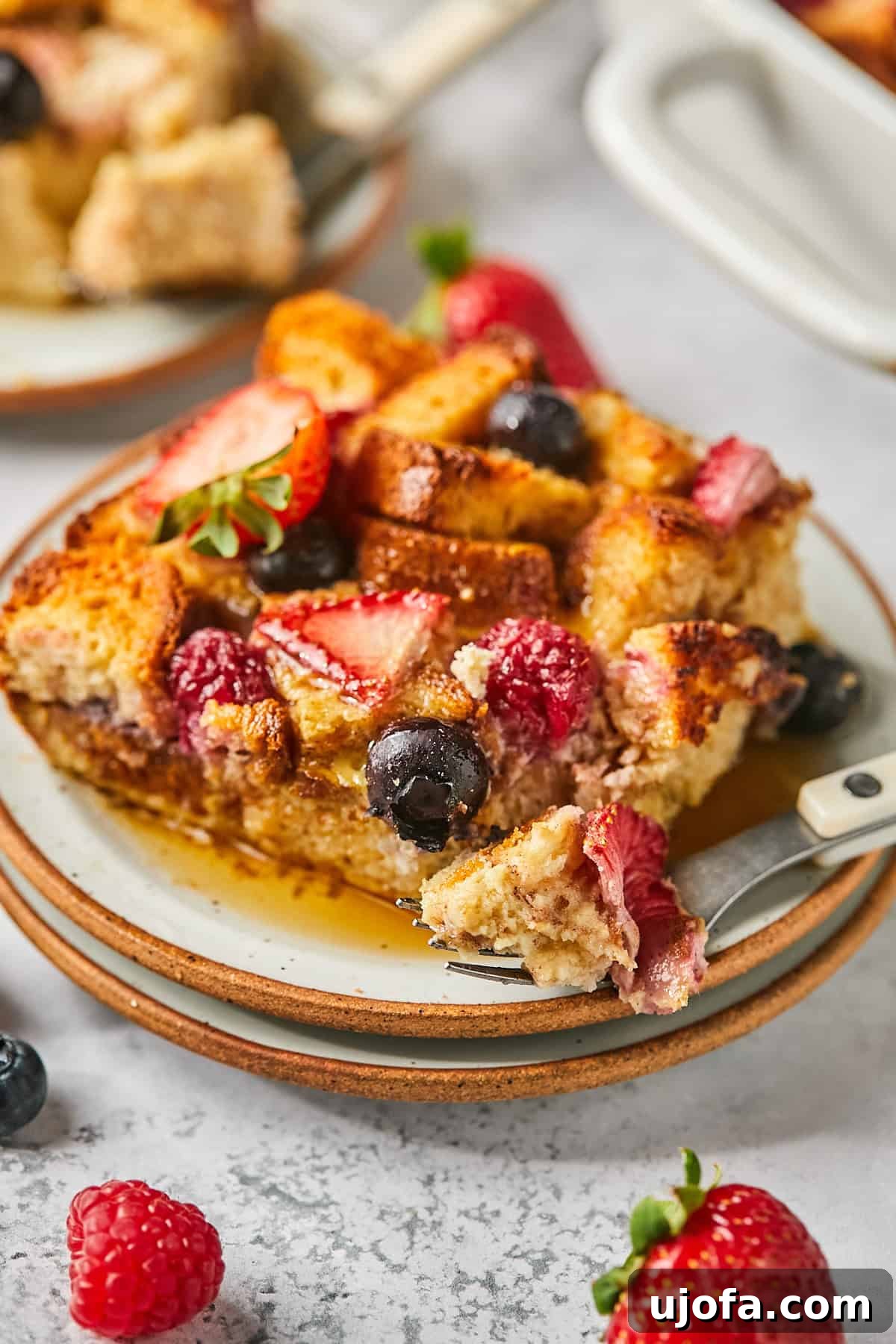 A fork holding a delicious bite of French toast casserole, drizzled with syrup and adorned with a fresh strawberry, capturing the essence of a perfect breakfast.