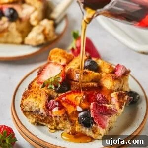Maple syrup being generously poured over a serving of protein French toast casserole, adorned with fresh berries, highlighting its irresistible appeal.