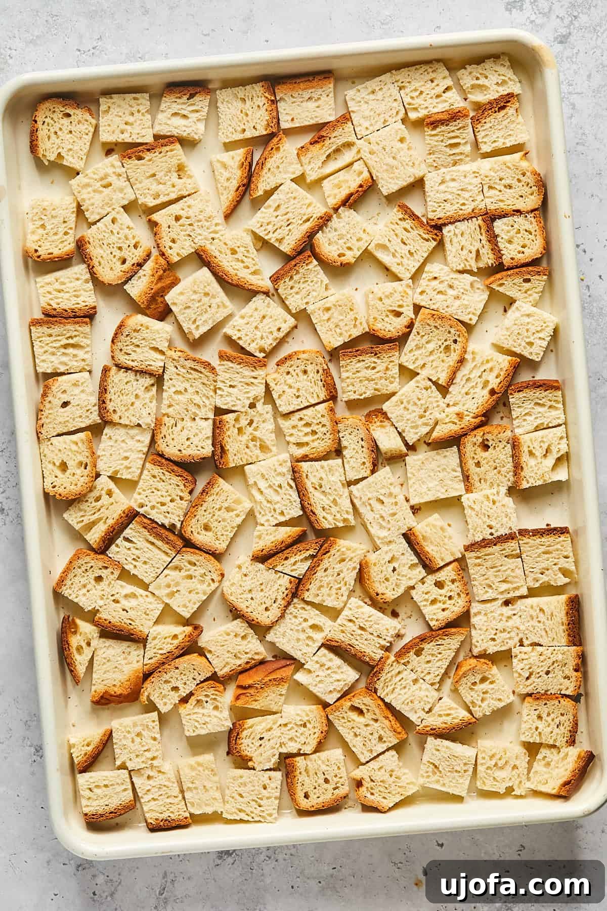 Cubed gluten-free bread spread evenly on a baking sheet, ready for toasting.