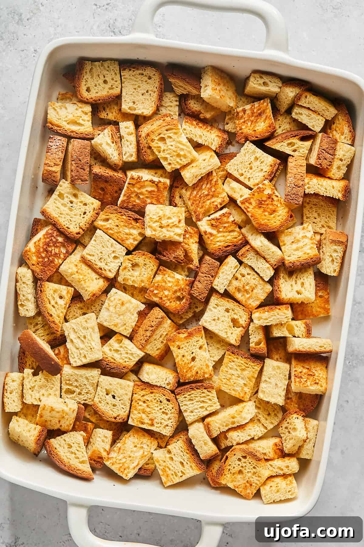 Toasted bread cubes neatly arranged in a 9x13-inch casserole dish, forming the base of the French toast bake.