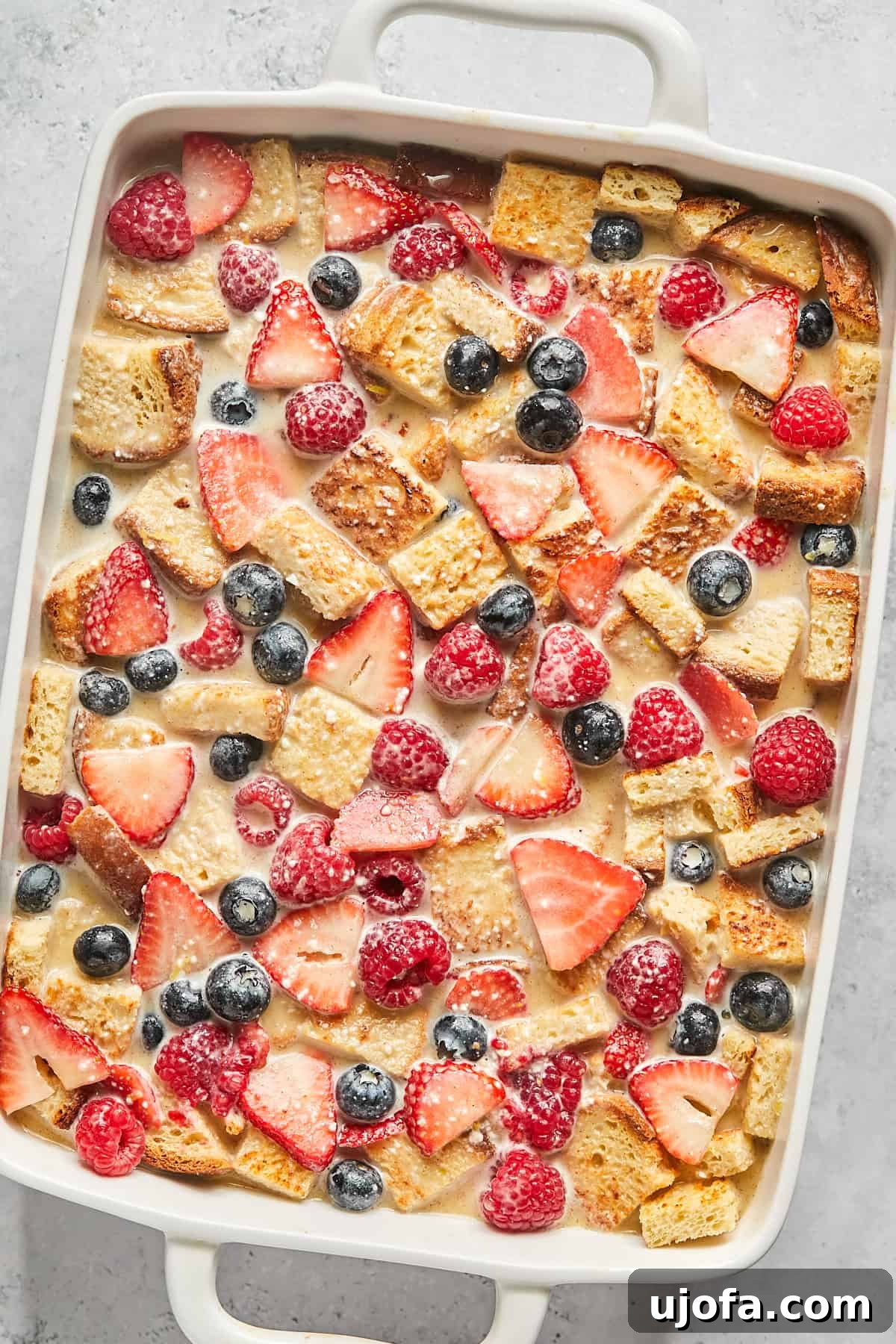 An unbaked overnight French toast casserole, with bread and berries thoroughly soaked in the rich custard mixture.
