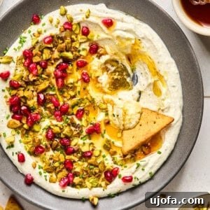 whipped feta with hot honey, pomegranates, and pistachios on a gray plate with a triangle pita chip in the middle