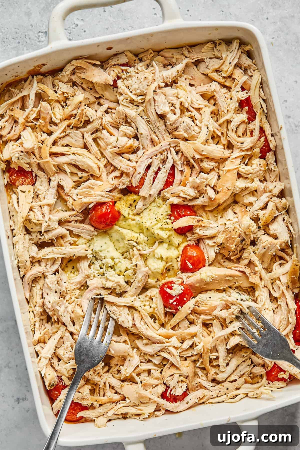 Dreamy Boursin Chicken Bake 10 two forks shredding the chicken in a casserole dish