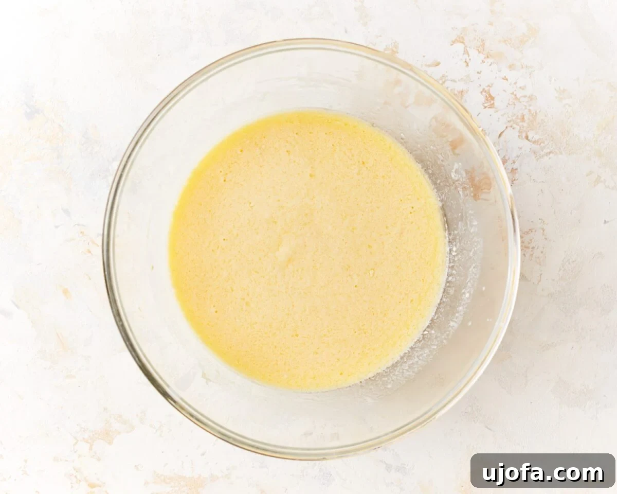A glass mixing bowl filled with a smooth, pale yellow liquid mixture of eggs, buttermilk, sour cream, melted butter, oil, and vanilla extract.