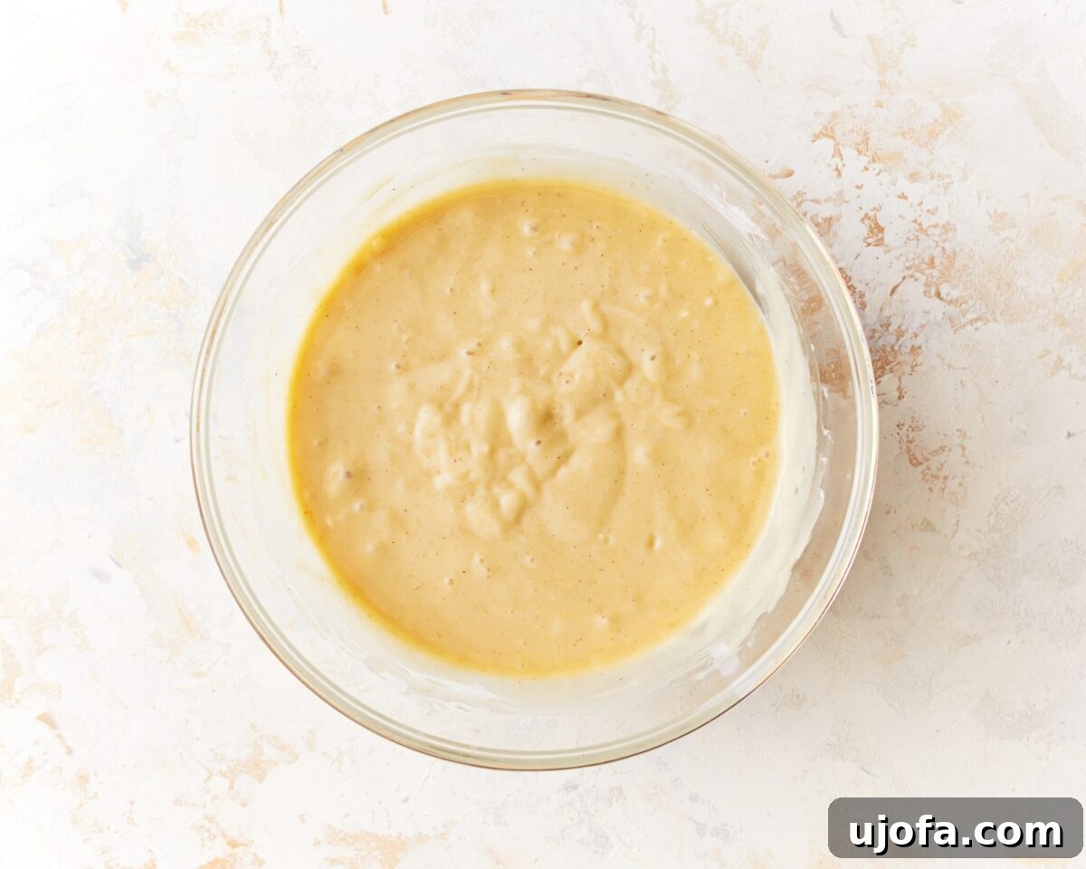 A glass mixing bowl with fully mixed muffin batter—thicker and creamier in texture, with visible small lumps from folded-in mix-ins.