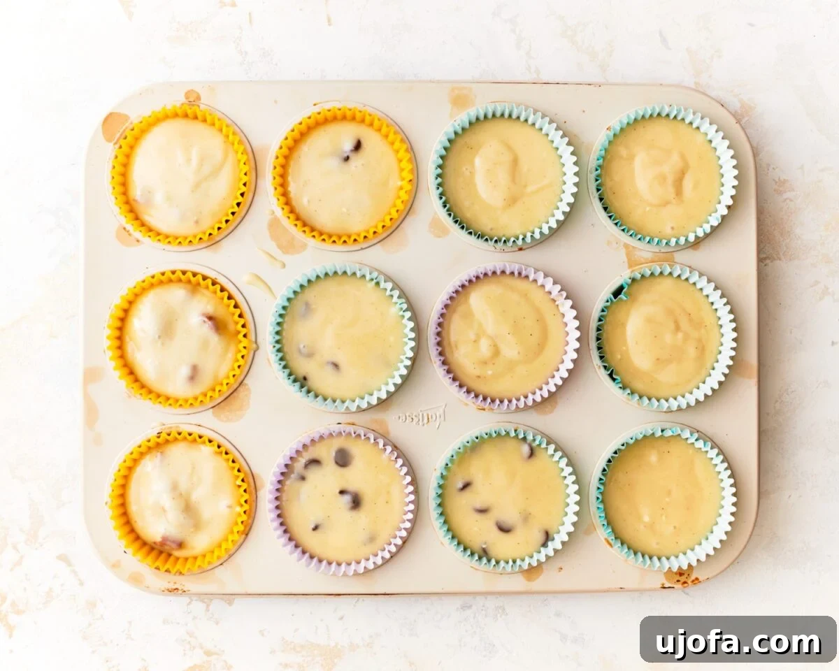 A muffin pan lined with colorful paper liners, each filled about three-quarters full with the gluten-free muffin batter, some showing chocolate chips.