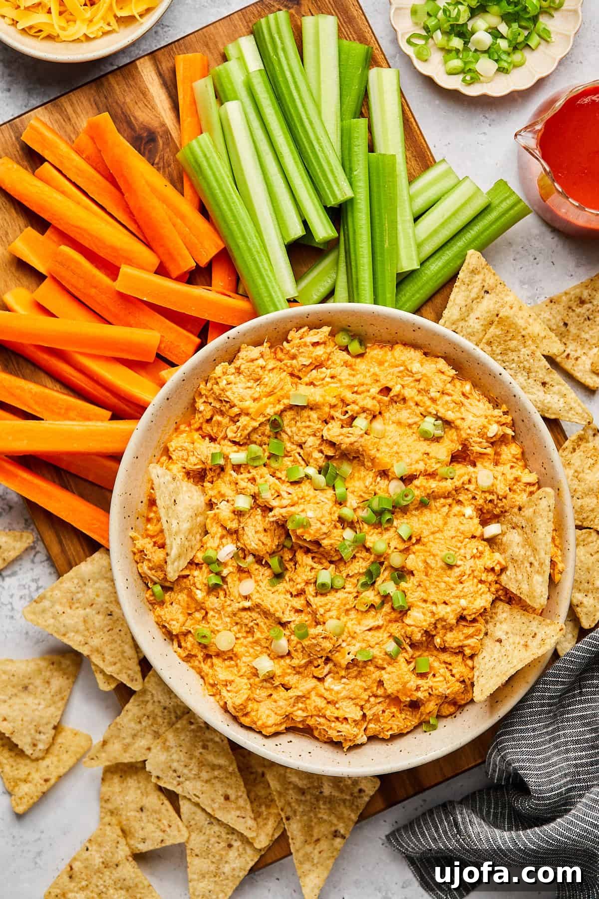 a bowl of high protein buffalo chicken dip surrounded by tortilla chips and veggies. 
