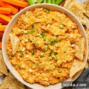 buffalo chicken dip in a white bowl with chips dipping in surrounded by chips and veggies.