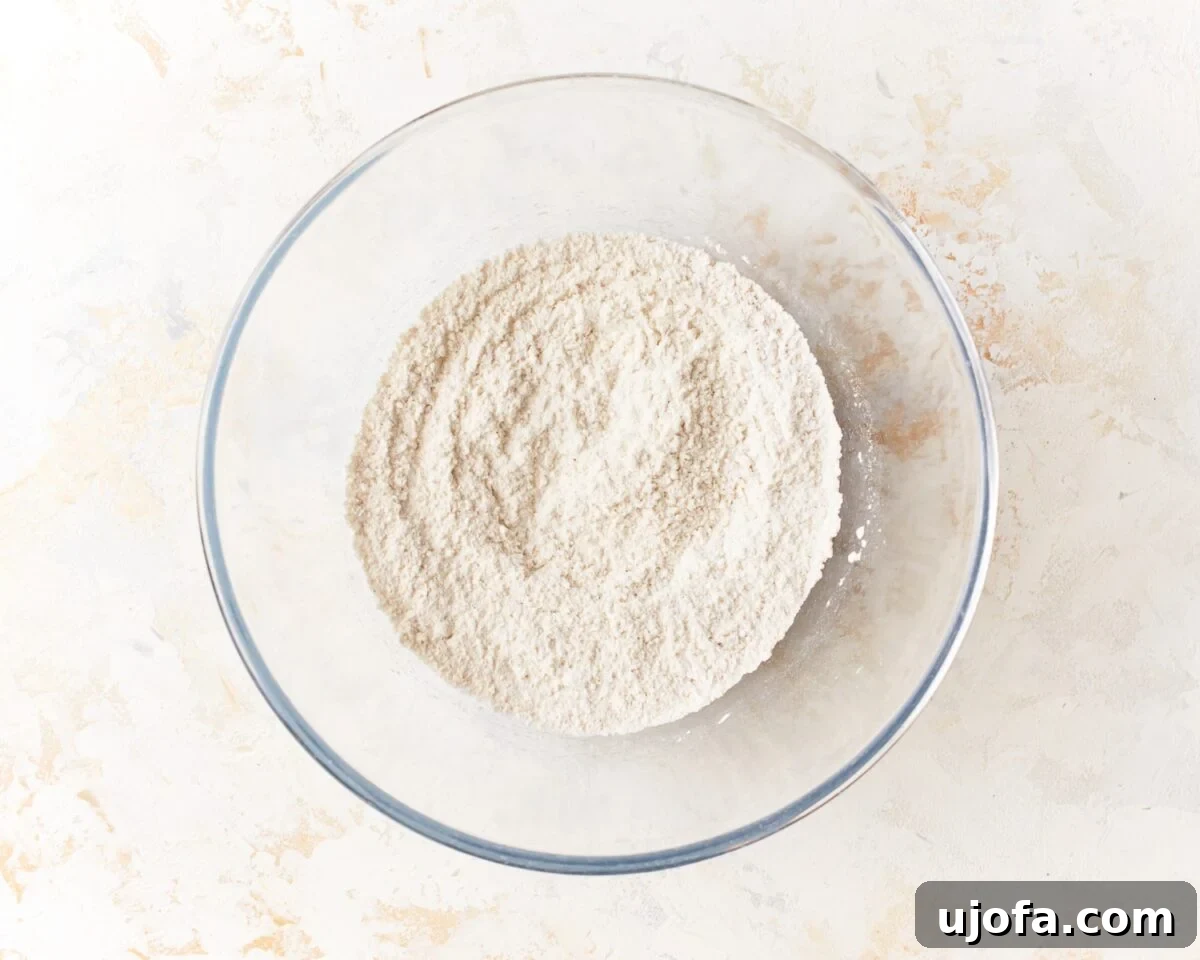 Glass mixing bowl filled with whisked dry ingredients for gluten-free pita bread on a light textured background.