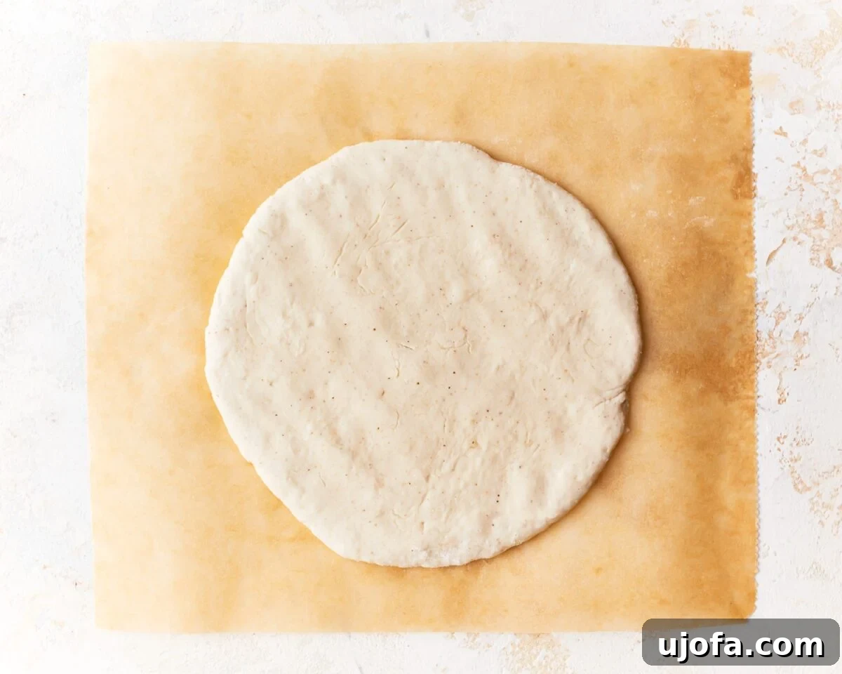 Flattened round of gluten-free pita dough shaped and ready to bake on a sheet of parchment paper.