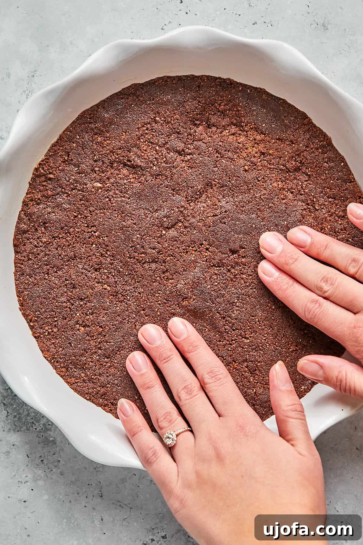 No-Bake Vegan Peanut Butter Bliss 7 Hands pressing the chocolate cookie and butter mixture into a pie pan to form the crust.