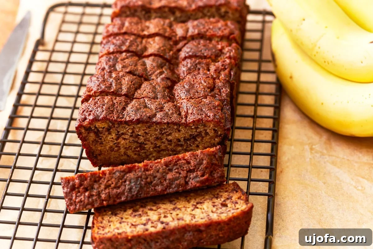 Tropical Coconut Banana Bread 10 A sliced loaf of coconut flour banana bread on a cooling rack, with ripe bananas in the background. The bread has a golden-brown crust and a moist, dense texture.