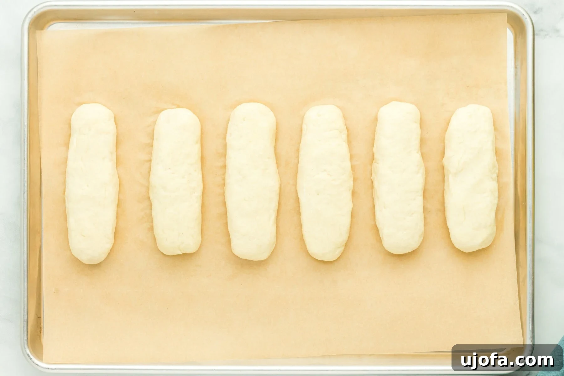 Gluten-free hot dog bun dough shaped into logs arranged on a parchment-lined baking sheet.
