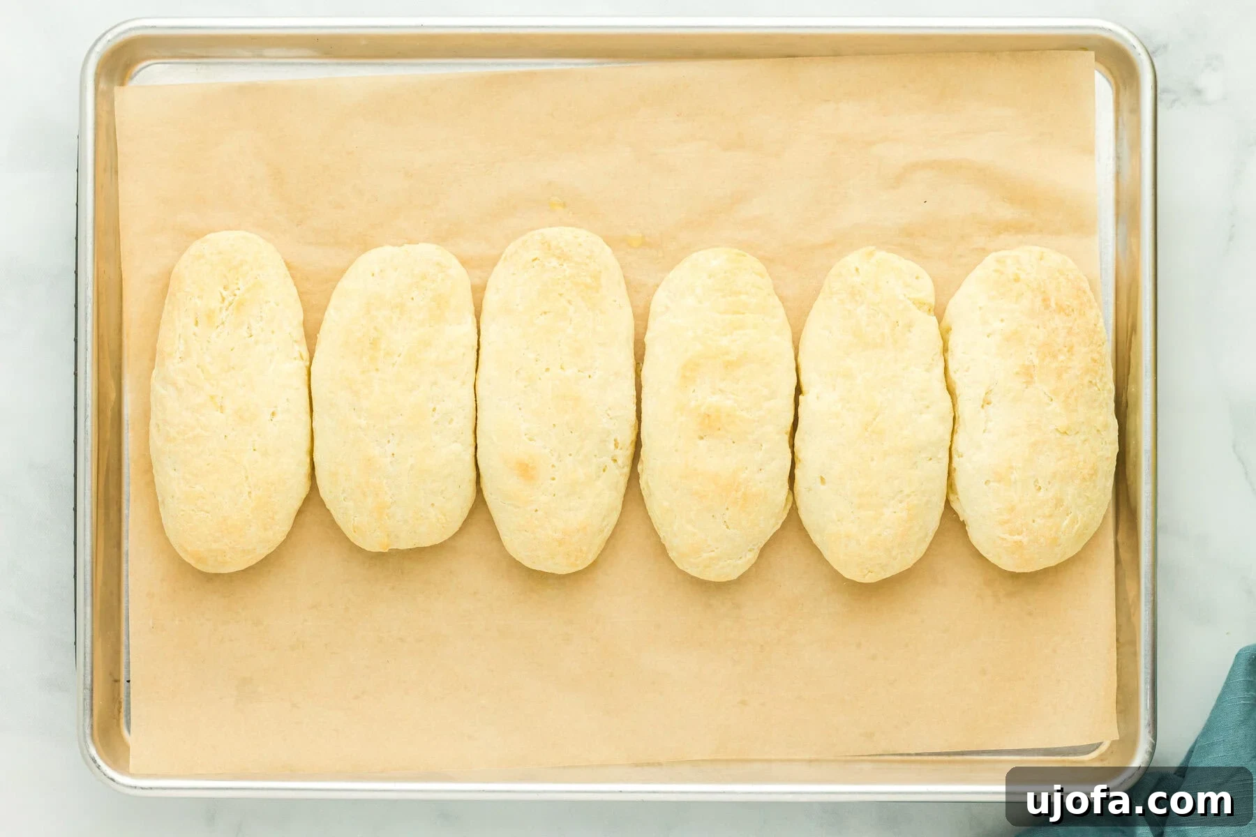 Baked gluten-free hot dog buns on a parchment-lined baking sheet, golden brown and perfectly risen.