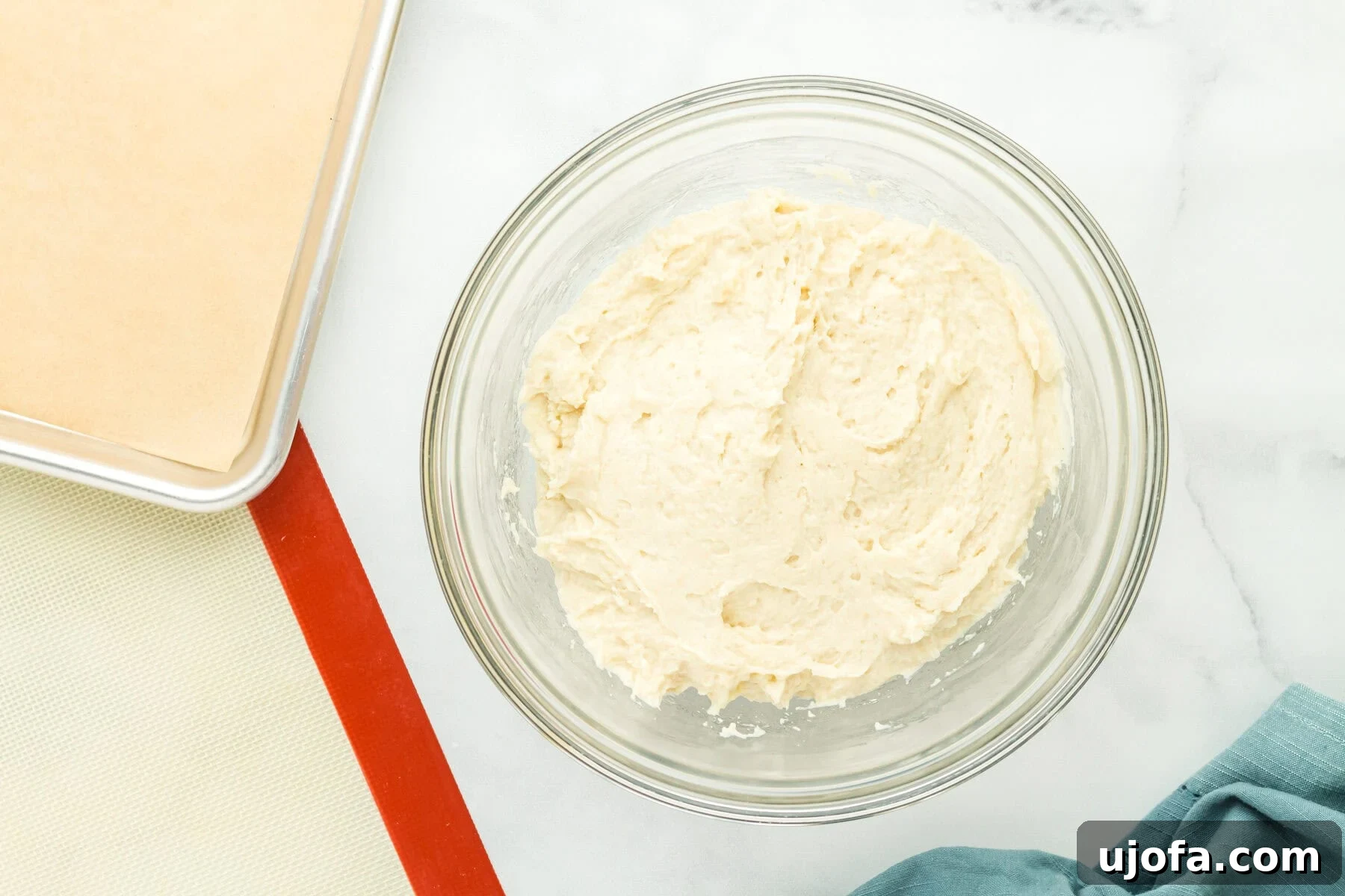 Gluten-free hot dog bun dough being mixed in a glass mixing bowl with an electric mixer.