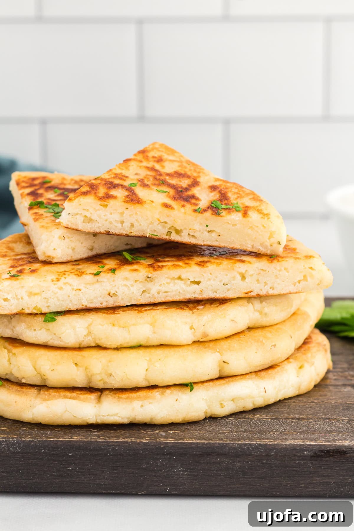Effortless Gluten-Free Flatbread 2 cut gluten-free flatbread stacked on a wooden cutting board, garnished with fresh herbs