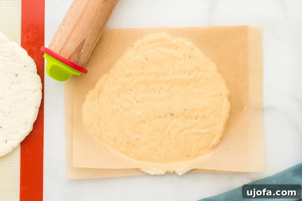 Effortless Gluten-Free Flatbread 10 gluten-free flatbread dough rolled out between pieces of parchment paper with a rolling pin in the upper corner