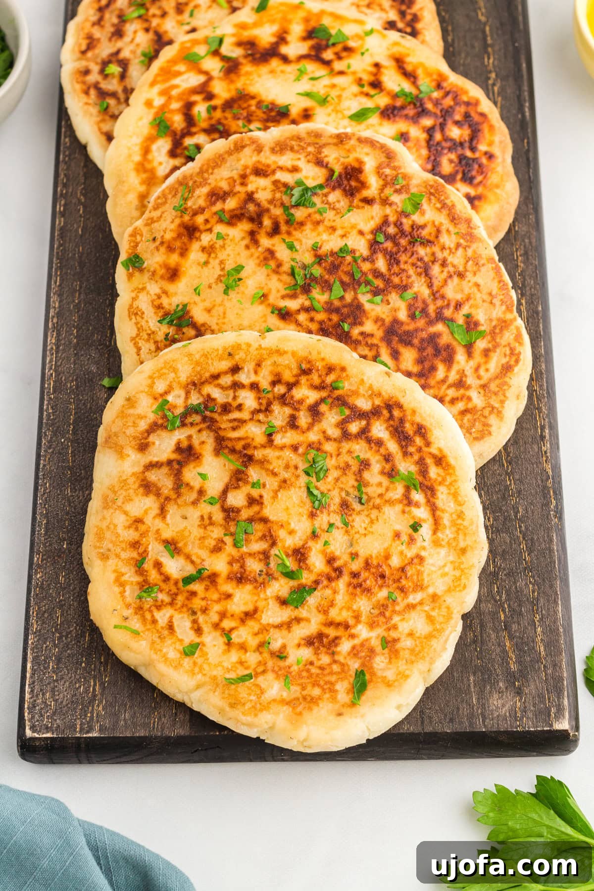 Effortless Gluten-Free Flatbread 4 four golden-brown gluten-free flatbreads on a black serving platter with fresh parsley