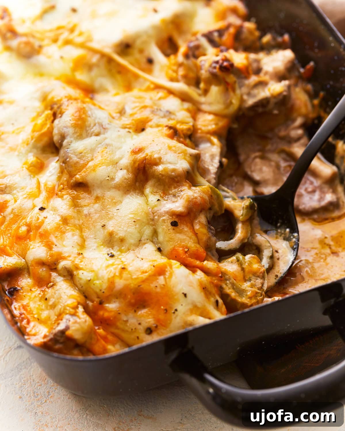 Close-up of a spoon scooping a generous portion of Philly Cheesesteak Casserole from a baking dish, highlighting the melted cheese and tender steak.