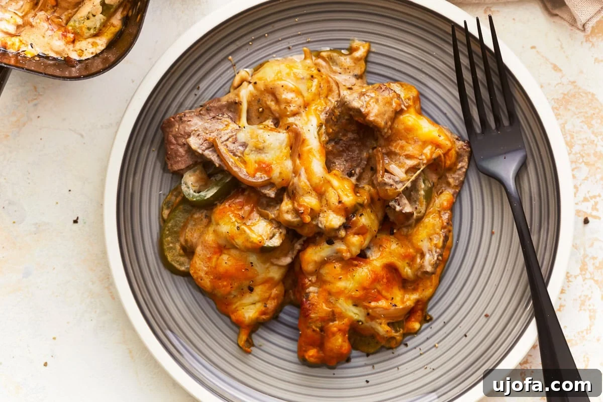 Overhead view of a serving of Philly Cheesesteak Casserole on a gray plate with a fork, ready to eat.