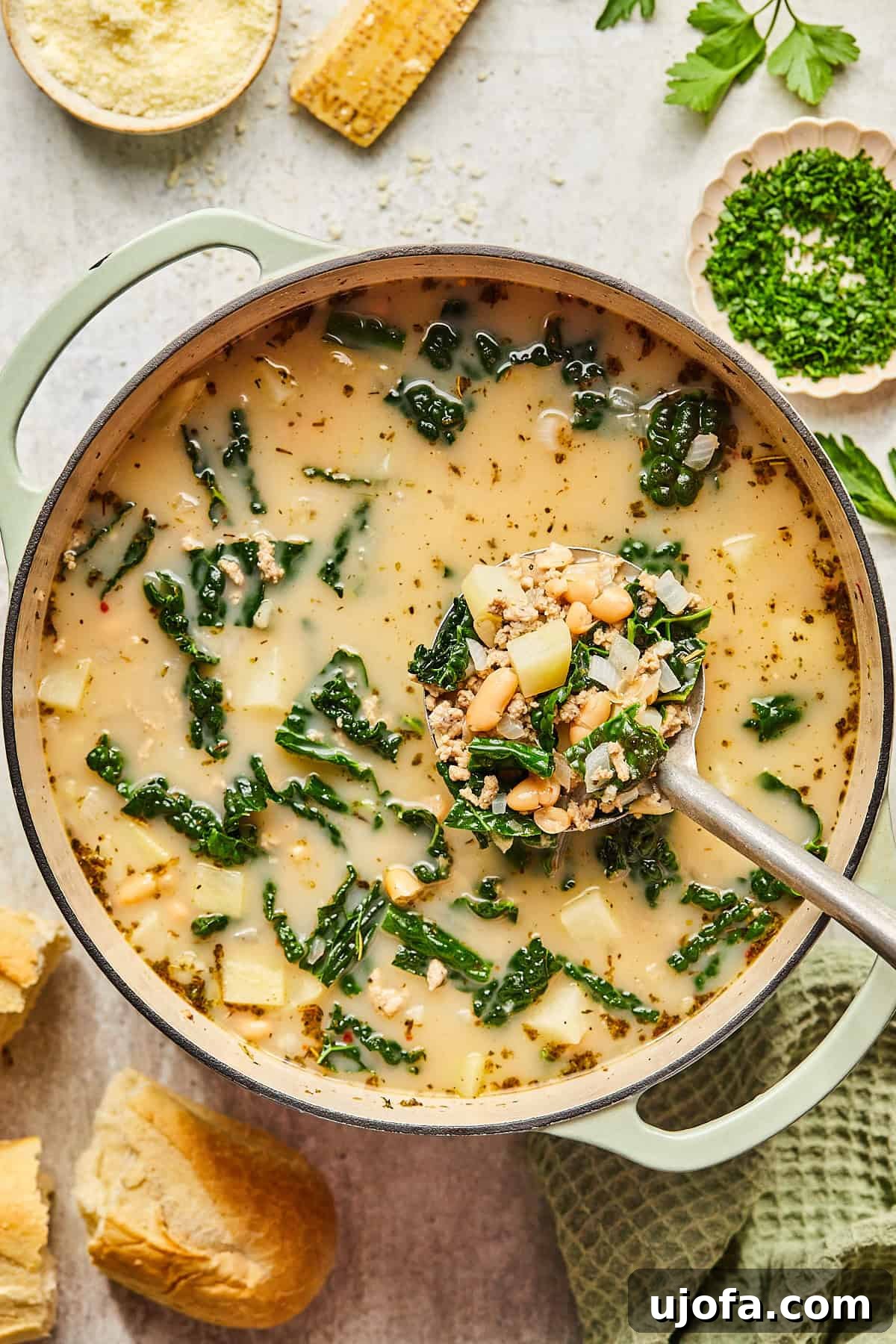 A large pot of freshly made sausage, kale, and white bean soup, with a ladle resting inside, ready to be served.