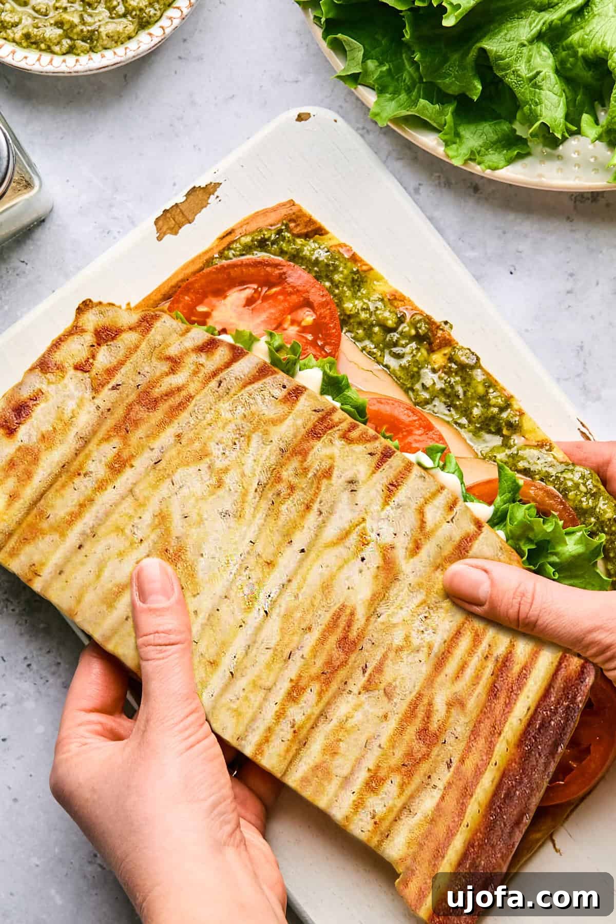 High Protein Cottage Cheese Flatbread Gluten Free Flourless 2 A delicious cottage cheese flatbread sandwich filled with fresh turkey, ripe tomatoes, crisp lettuce, and vibrant pesto, held by two hands on a rustic cutting board.