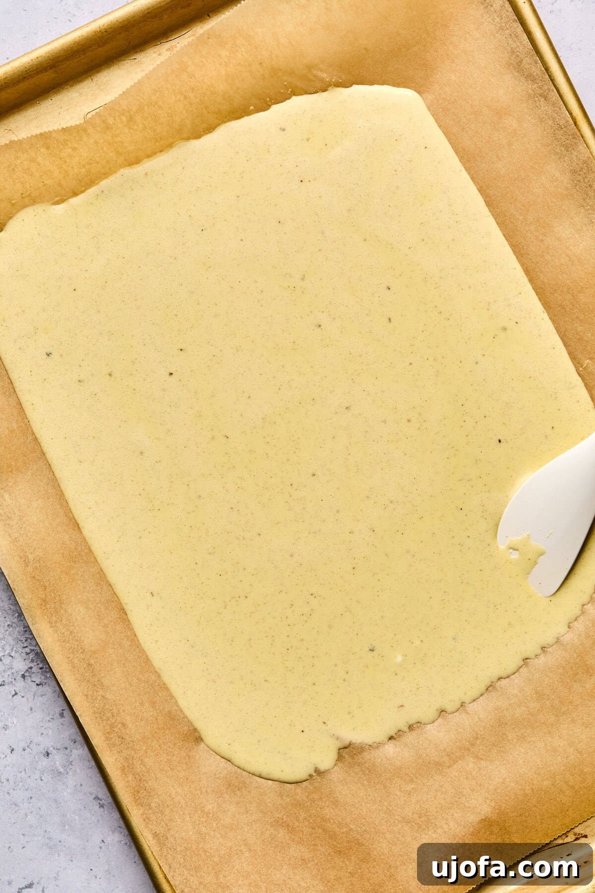 High Protein Cottage Cheese Flatbread Gluten Free Flourless 6 The liquid cottage cheese flatbread batter being spread thinly onto a parchment-lined baking sheet with a white spatula.