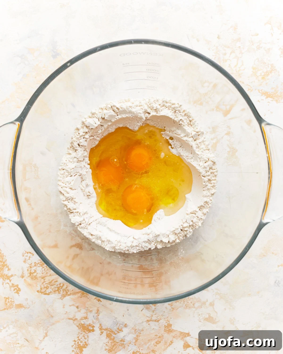 eggs in the center of a flour well in a glass bowl.