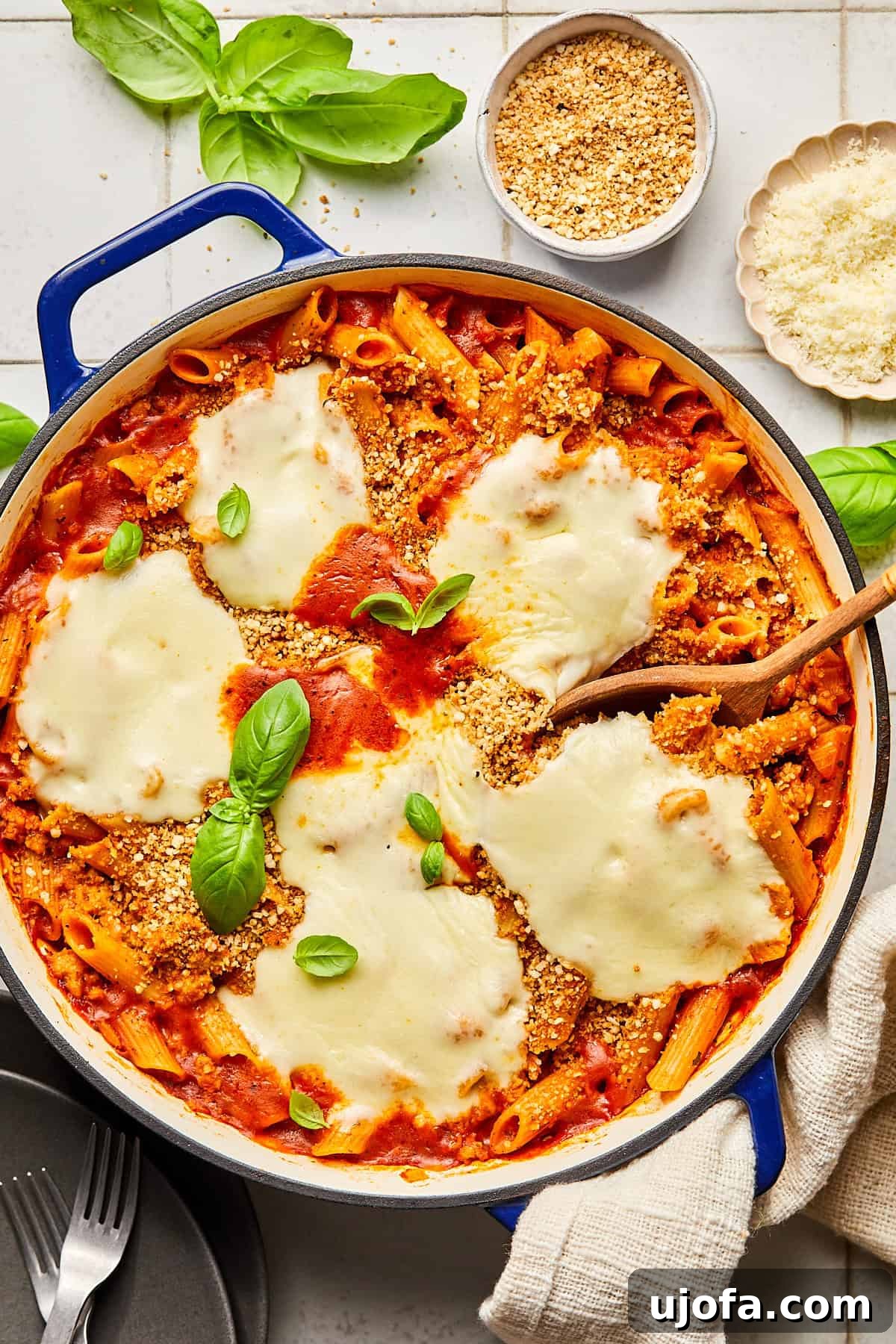 chicken parmesan pasta in a blue dutch oven surrounded by basil and ingredients