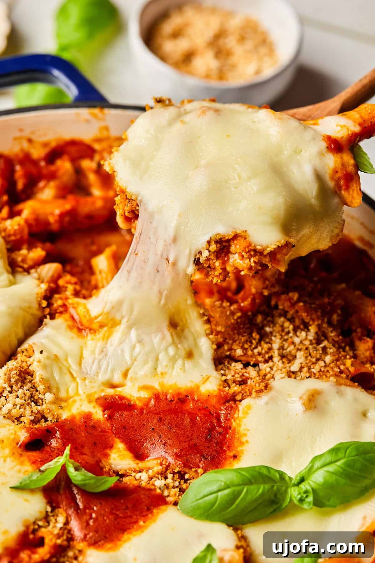 a spoon pulling a cheesy bite out of chicken parmesan pasta
