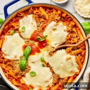 chicken parmesan pasta in a blue dutch oven surrounded by basil and ingredients