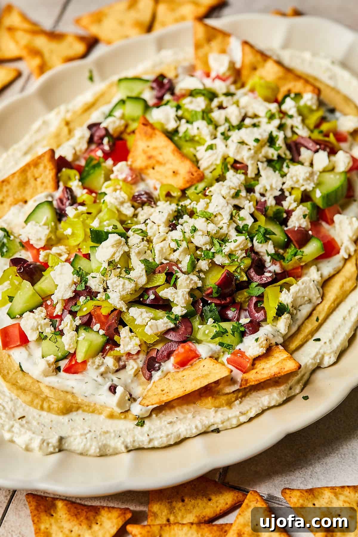 A close-up side view of the layered Greek dip, showcasing the distinct, colorful layers of feta, hummus, tzatziki, and fresh vegetables.