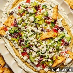 A vibrant 7-layer Greek dip on a platter, surrounded by golden pita chips.